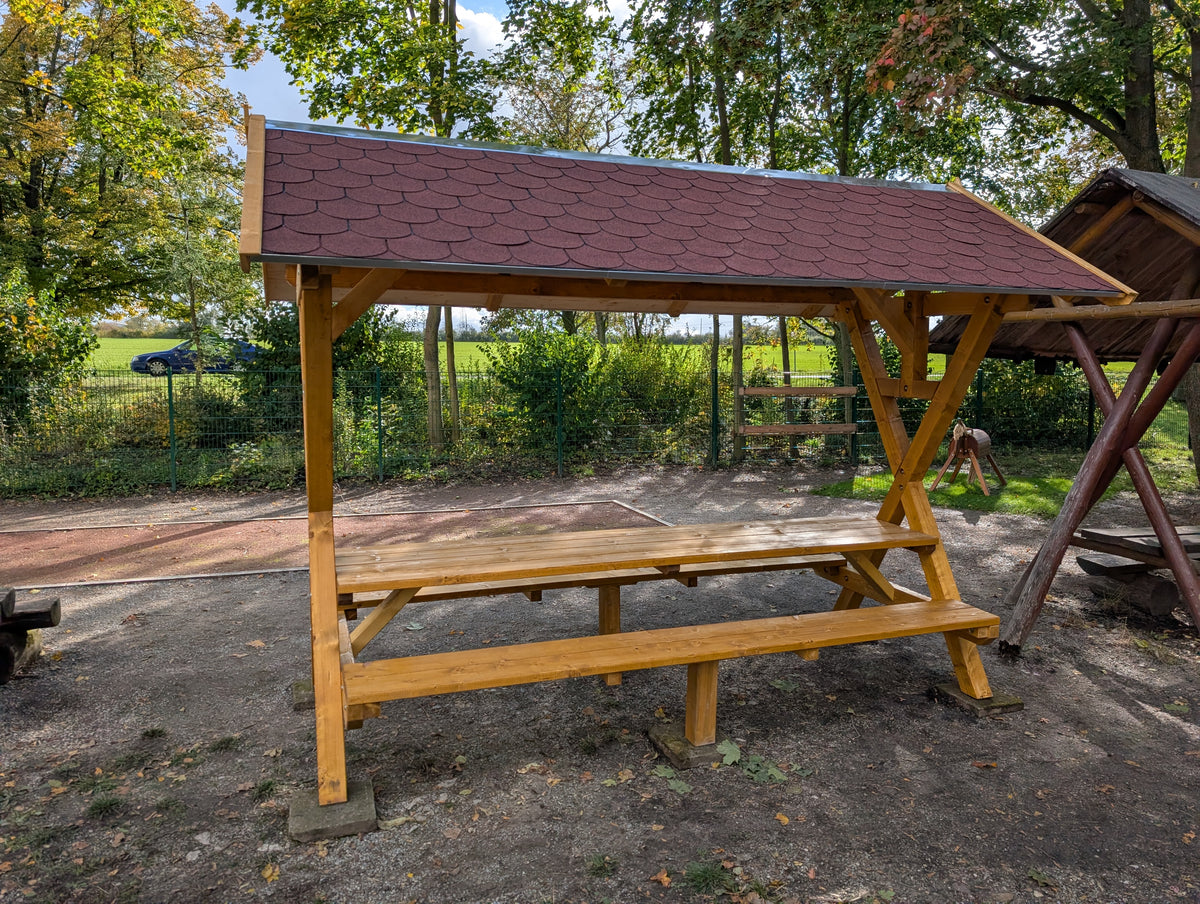 Waldschänke Premium XXL aufgebaut auf einem Spielplatz – überdachte Sitzgruppe mit Tisch und Bänken